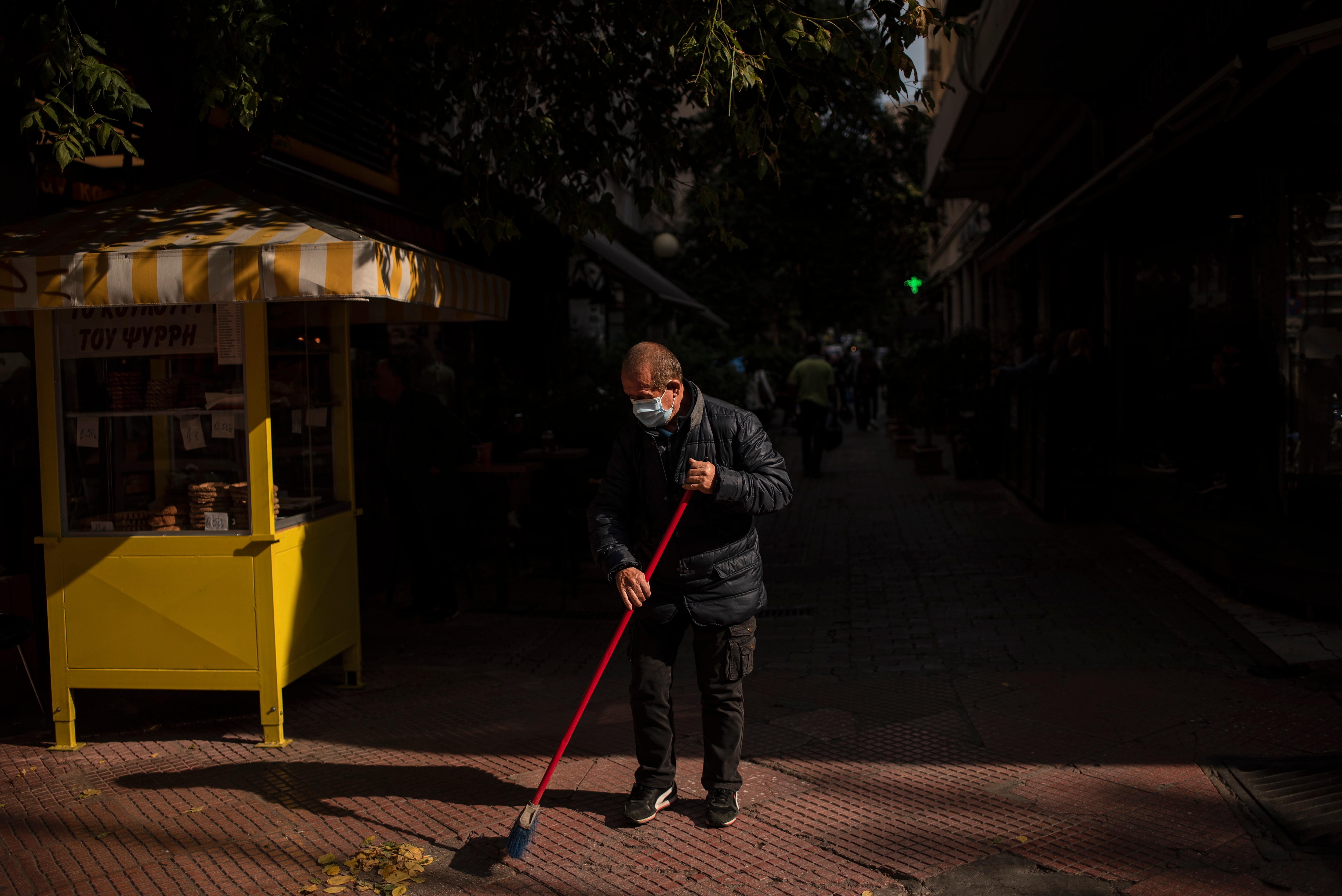 رجل يرتدي قناعًا وقائيًا ينظف شارعًا في الحي التجاري الرئيسي بأثينا في اليونان في 30 أكتوبر.