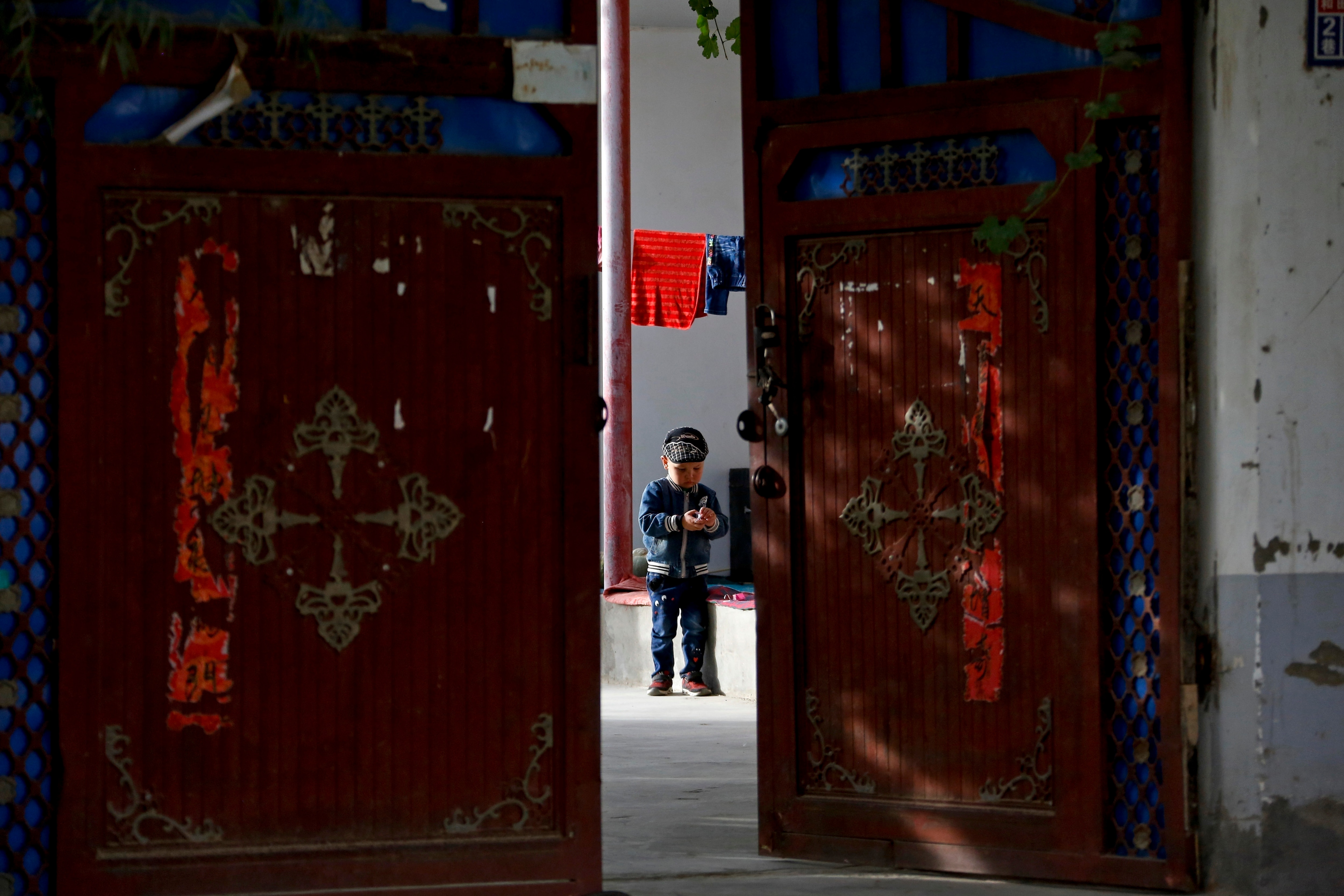 A Uighur child plays alone in the courtyard of a home at the Unity New Village in Hotan, in western China's Xinjiang region.