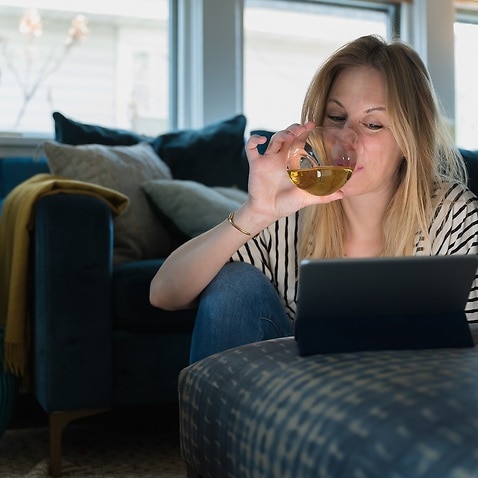 Woman drinking wine and looking at tablet at home