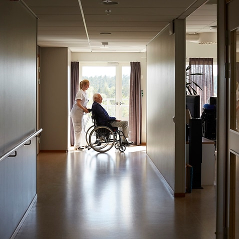 Full length side view of female nurse pushing senior man on wheelchair at hospital corridor