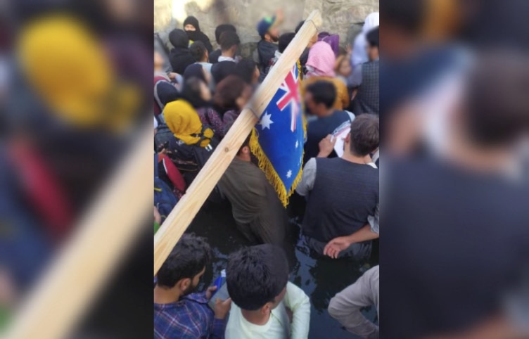 Former embassy guards stand in sewage water and raise an Australian flag outside Kabul airport to signal their location to officials.