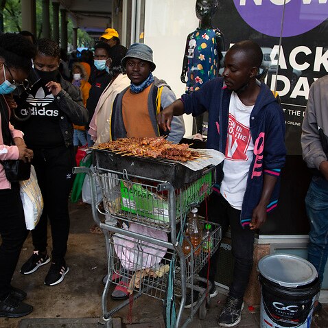 A masked shopper buys chicken on a crowded sidewalk in Pretoria, South Africa