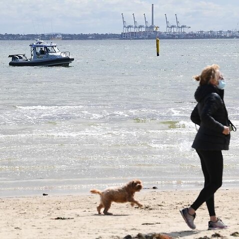 A masked woman walks along a Melbourne beach.