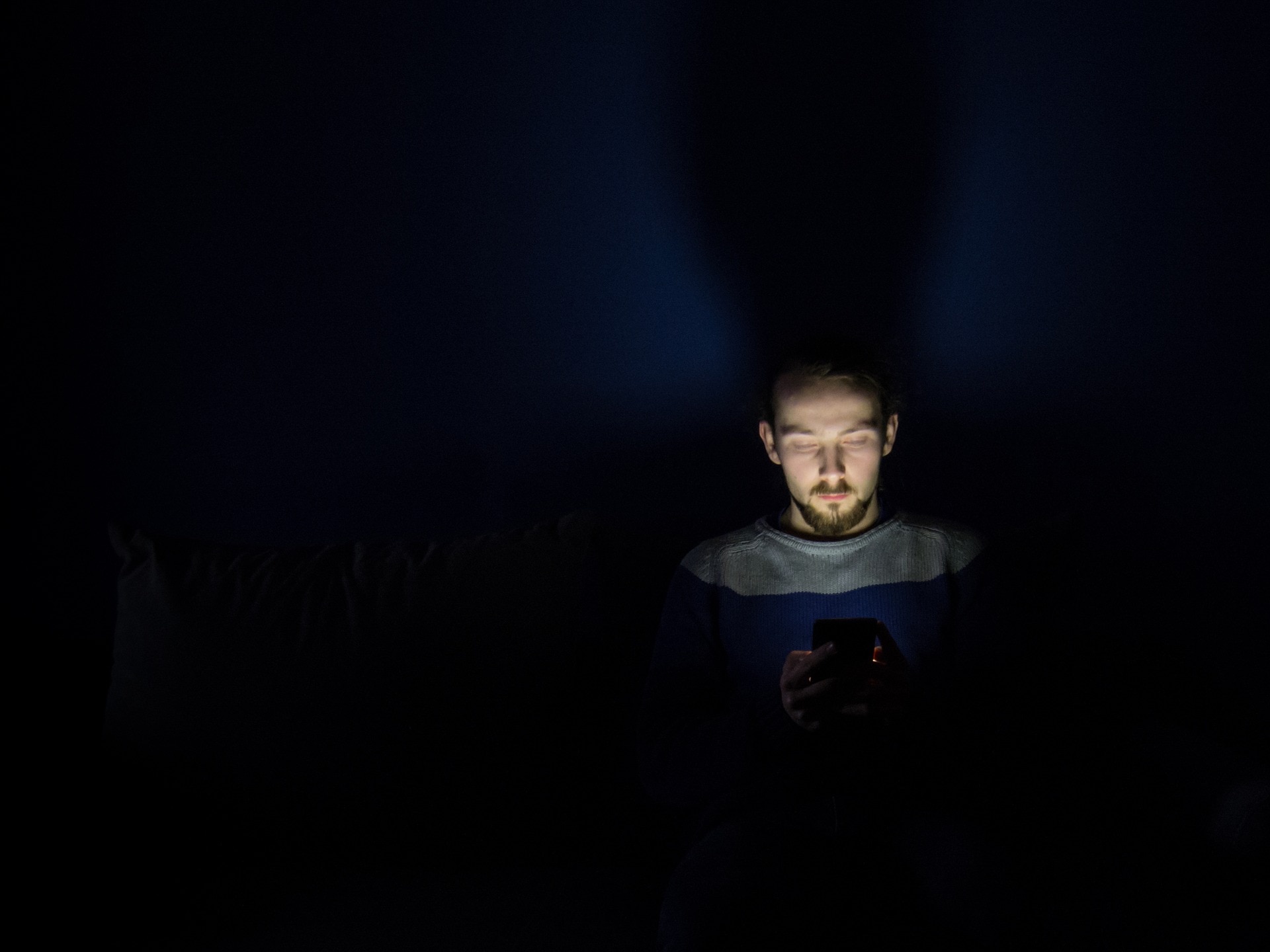 Image of a man using a mobile phone at night with visible blue light emitting from its screen.