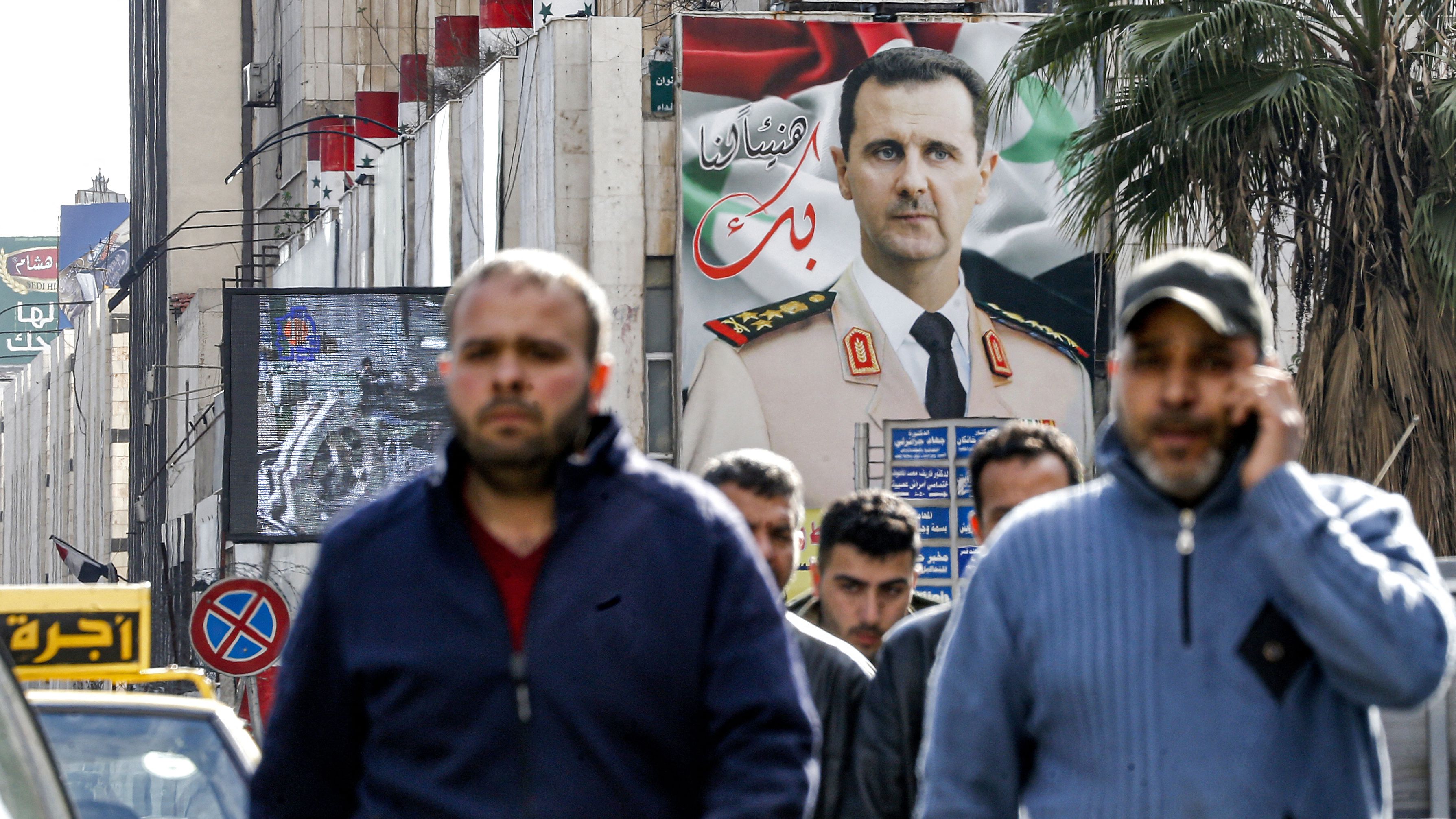 People walk before a giant billboard showing Syria's president Bashar al-Assad along a street in the capital Damascus on 15 December, 2021.