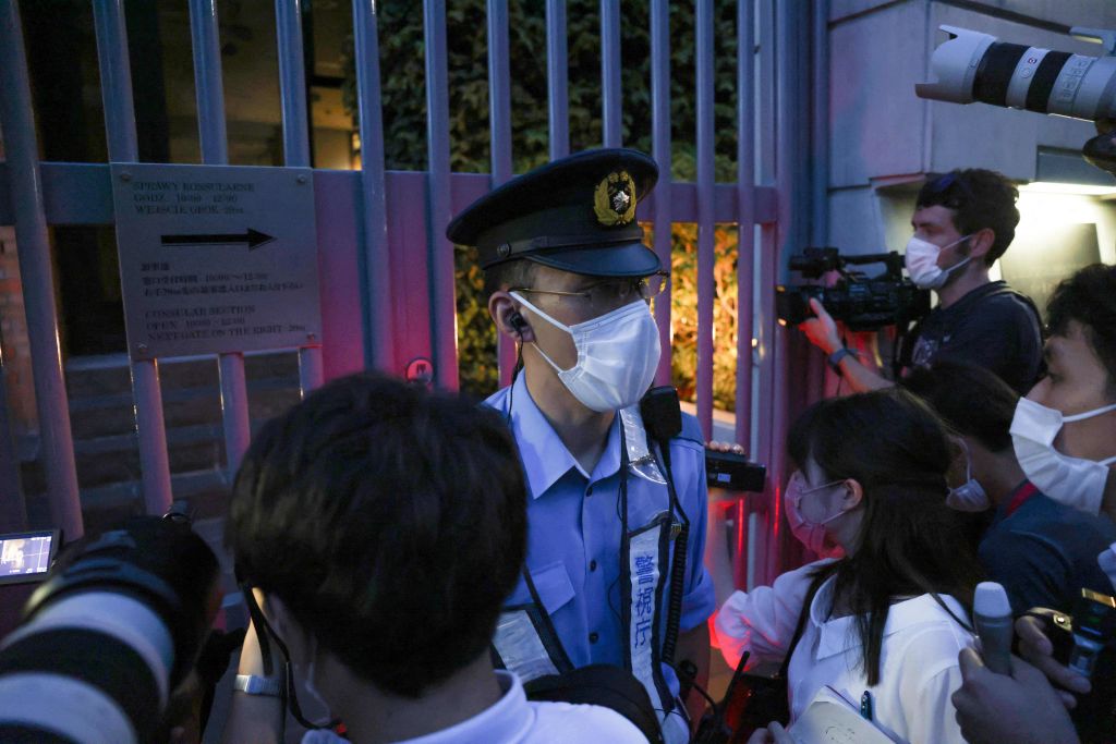 Policjant patrzy, jak dziennikarze gromadzą się przed bramami polskiej ambasady, gdzie ukrywa się białoruska lekkoatletka Kristina Simanuskaya.