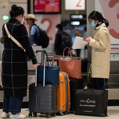File photo of passengers wearing protective masks collecting baggage after arriving on a flight at Sydney Airport. 