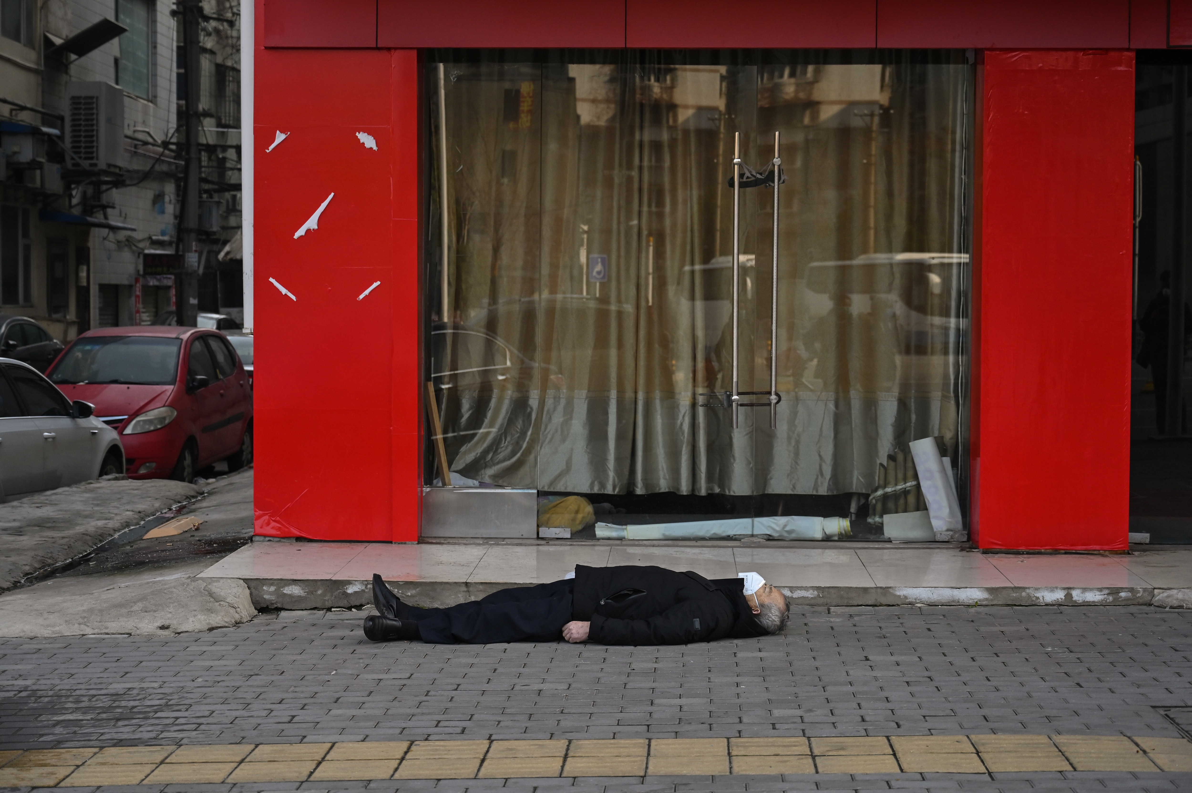 An elderly man wearing a face mask lying on the pavement after he collapsed and died near a hospital in Wuhan.