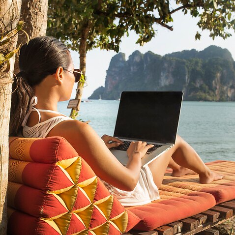 Woman using laptop computer while sitting on lounge chair against sea