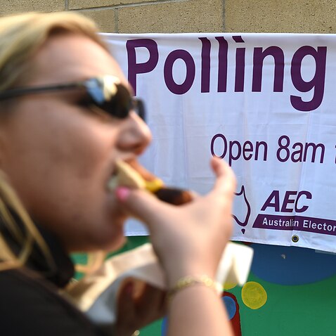 A voter eats a sausage as she lines up to cast her ballot in Brisbane, Saturday, July 2, 2016. About 15 million Australians will vote in today's federal election. (AAP Image/Dan Peled) NO ARCHIVING