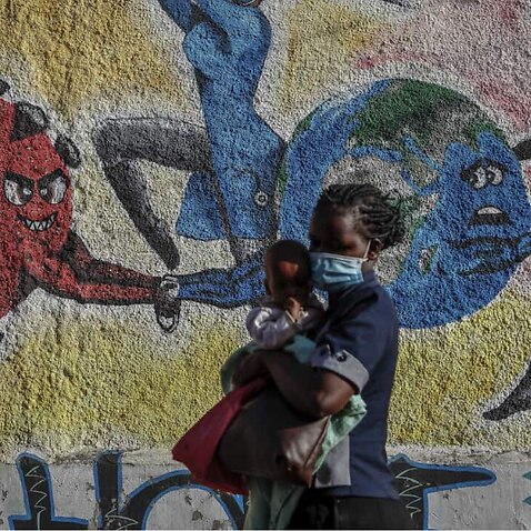 A woman and child walk past an informational mural portraying the global battle against the coronavirus, on a street in Kericho, Kenya.