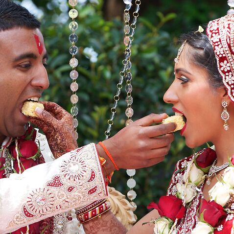 Bride and Groom feeding wedding cake to each other during an Indian wedding ceremony.