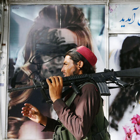 A Taliban fighter walks past a beauty salon with images of women defaced using spray paint in Kabul on August 18, 2021.