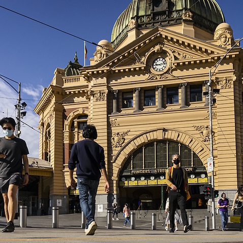 People are seen walking across Flinders Street in Melbourne, Friday, October 22, 2021.