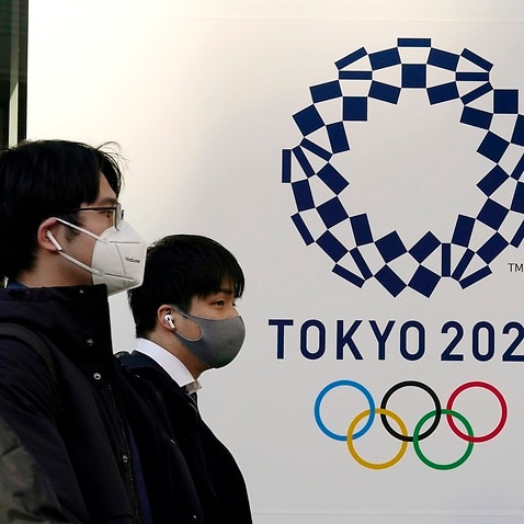 Pedestrians wearing protective masks walk past the emblem of Tokyo 2020 Olympic Games in Tokyo.