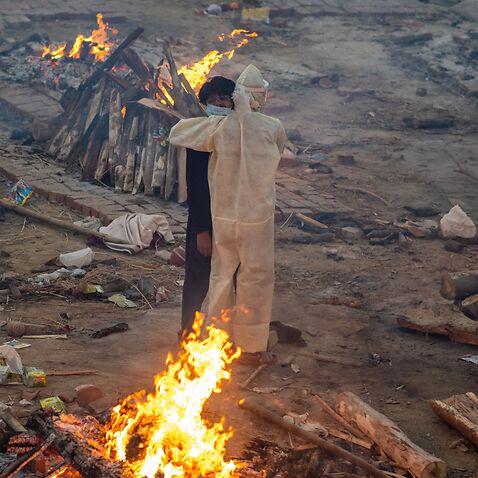 Family members embrace amid burning pyres of victims who lost their lives due to COVID-19 at a cremation ground in New Delhi on 26 April, 2021. 