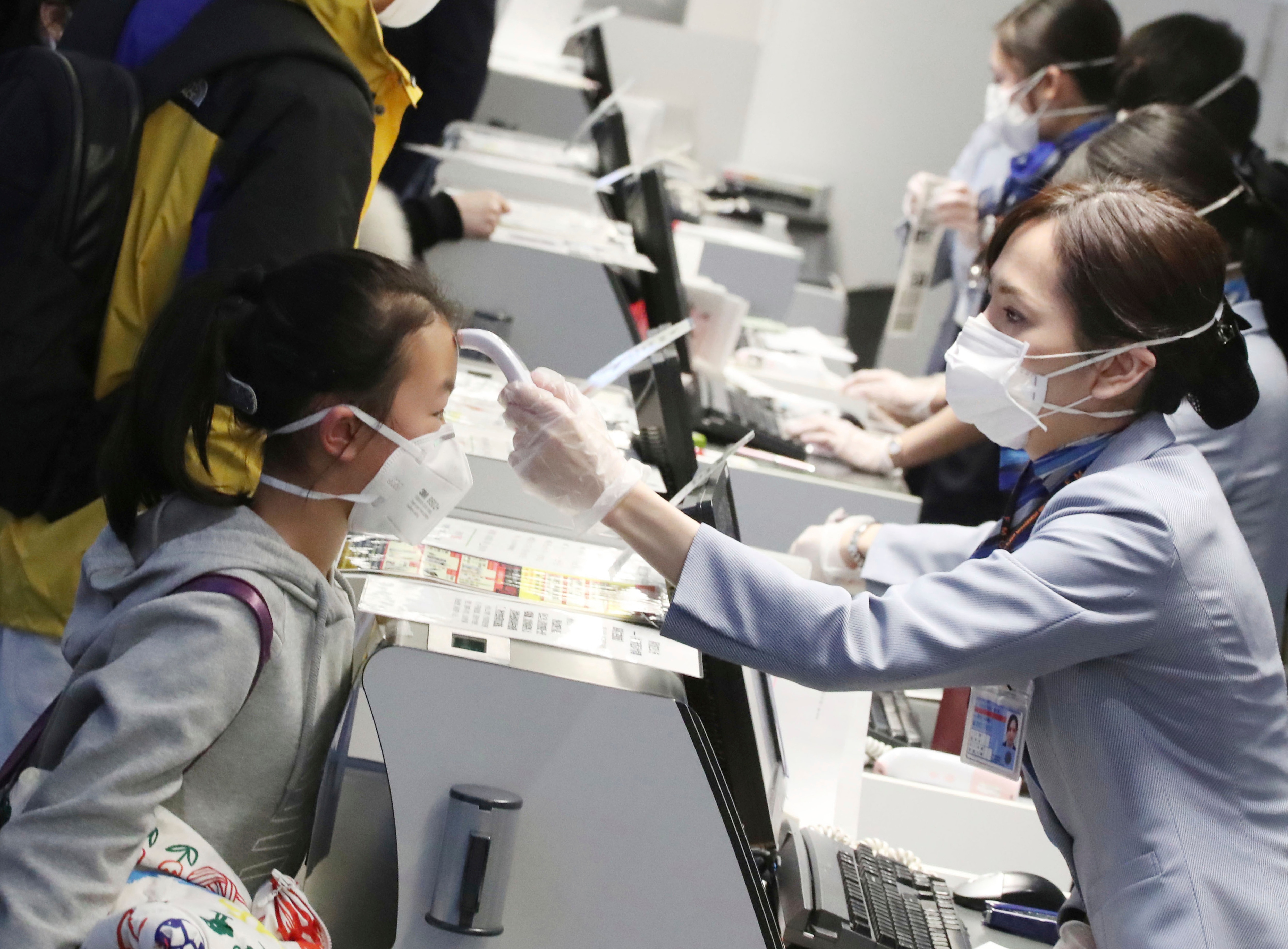 Passengers have their body temperature assessed by check-in staff ahead of a flight from Tokyo to the coronavirus epicentre of Wuhan, China.