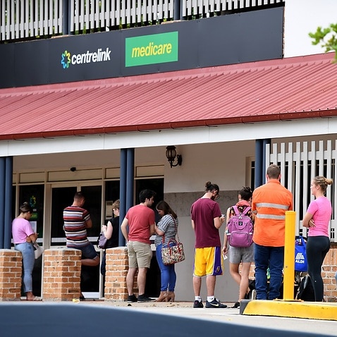 People are seen in a long queue outside a Centrelink office in Brisbane, 24 March 2020.