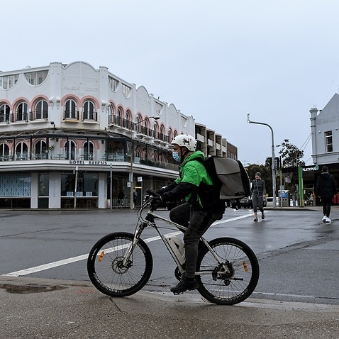 A food delivery driver wearing a face mask rides their bicycle through the empty streets of Bondi, Sydney on 14 July 2021. 