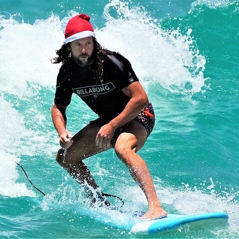 Tony O'Connor, originally from England, rides a surfboard while wearing a Santa hat as he celebrates Christmas at Bondi Beach in Sydney, Dec. 25, 2021.