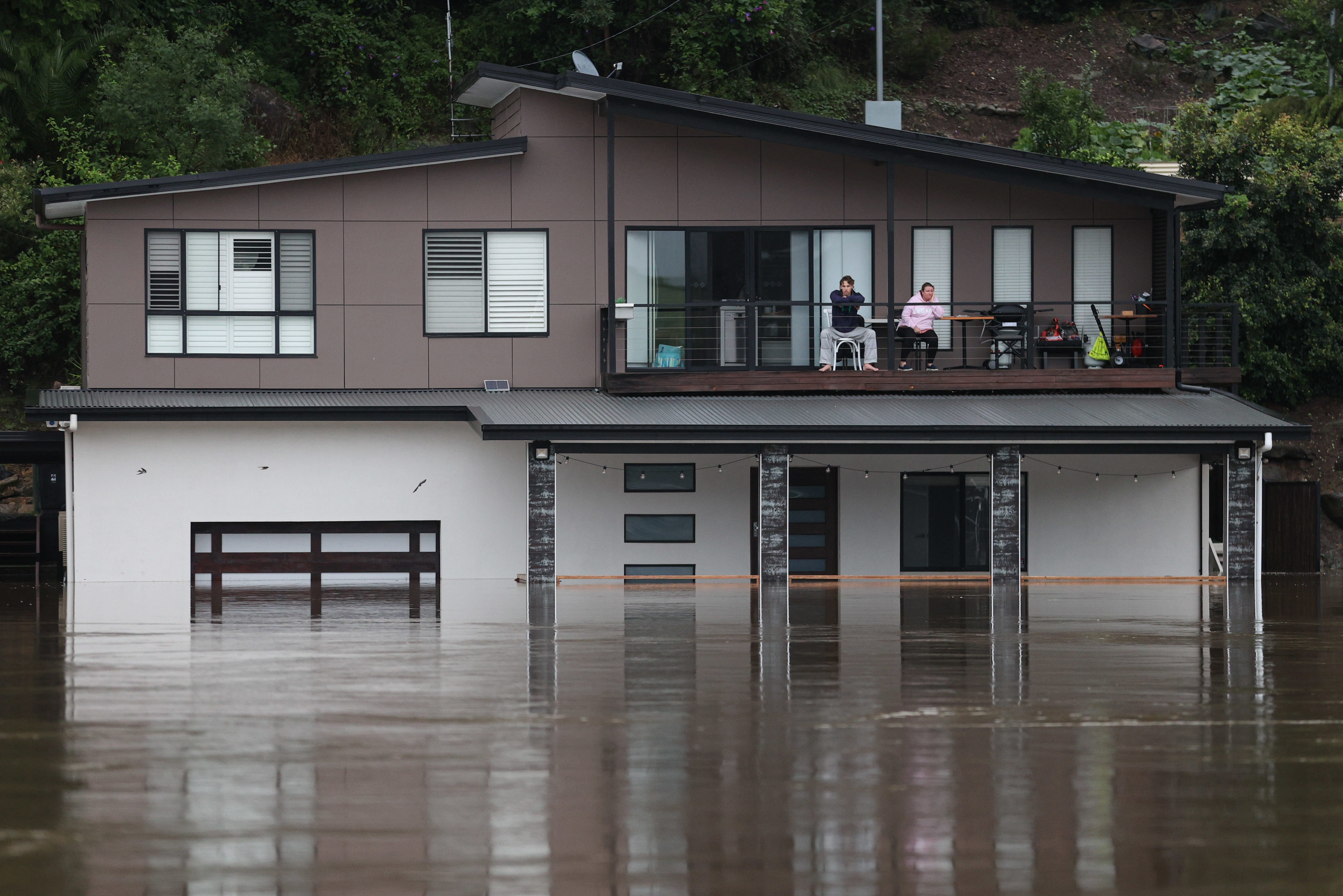 People look out at the swollen Hawkesbury River from the deck of a partially submerged house as floodwaters rise in western Sydney on 23 March.