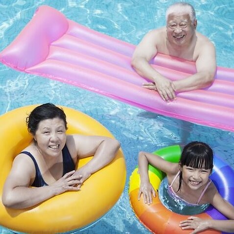 Multi-generational family playing in the pool with inflatable tubes, looking at camera