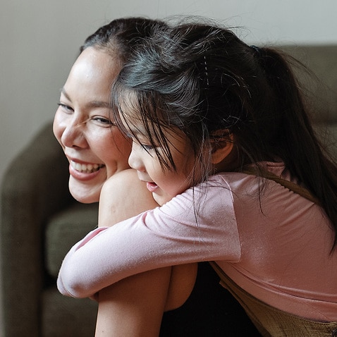 Young girl hugging mum from behind
