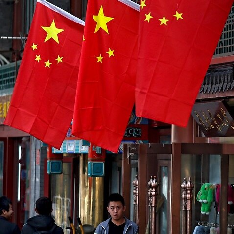 People walk by a worker waiting for customers outside his retail shop displaying national flags in the Chinese capital 