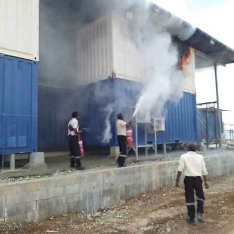Police and immigration officers can be seen extinguishing the fire at the Manus Island compound.