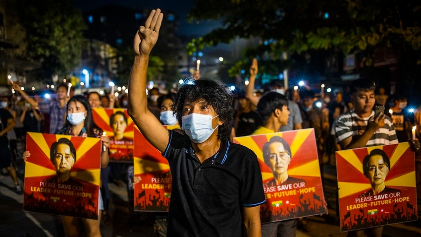 A man flashes the three-fingered gesture while others hold images of deposed Myanmar leader Aung San Suu Kyi during a candlelight night demonstration in Yangon.