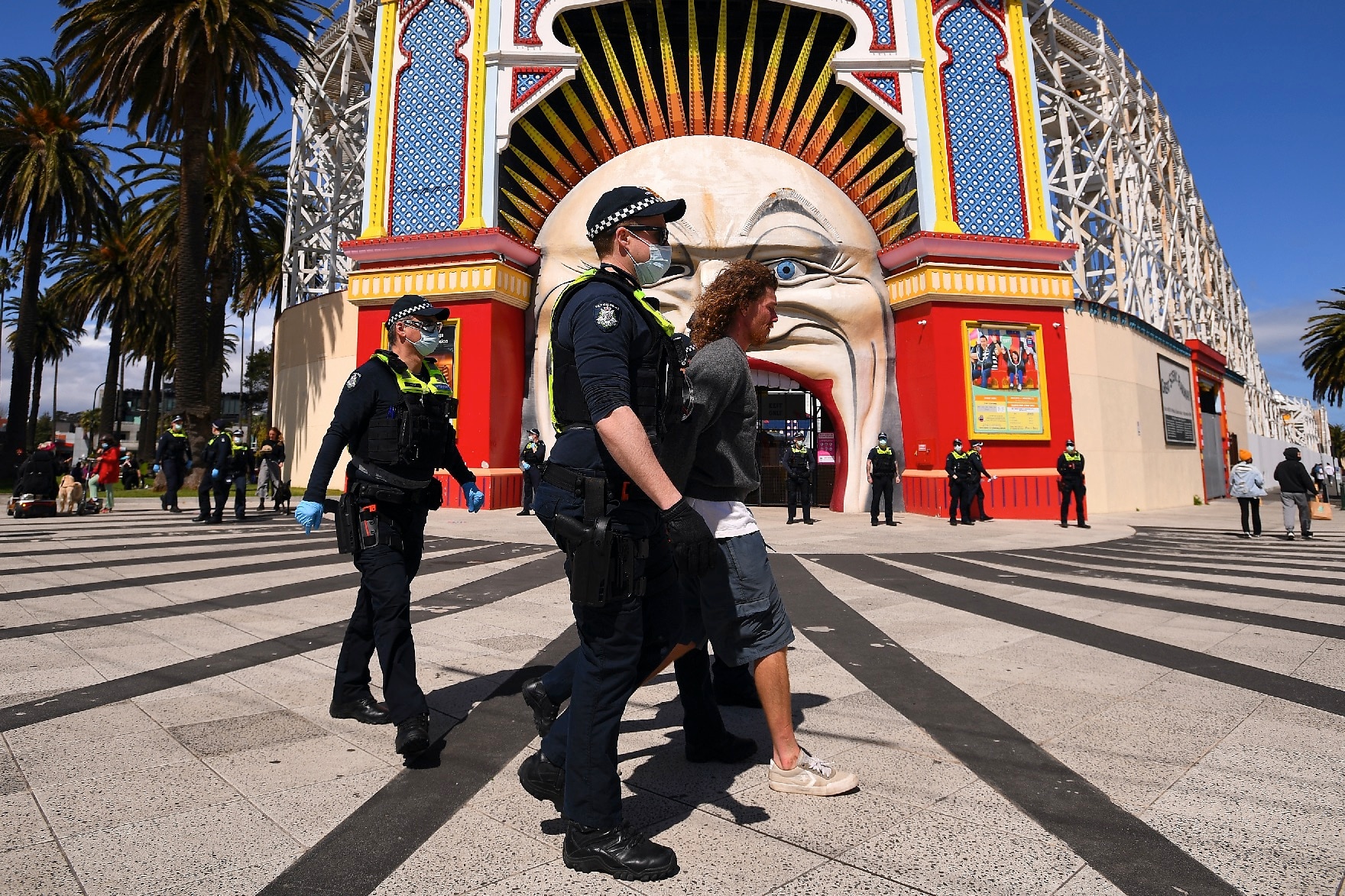 Victorian Police officers detain a person outside of Luna Park in Melbourne.