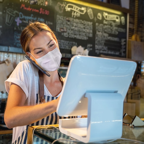 Waitress at a restaurant getting a delivery order on the phone and wearing a facemask