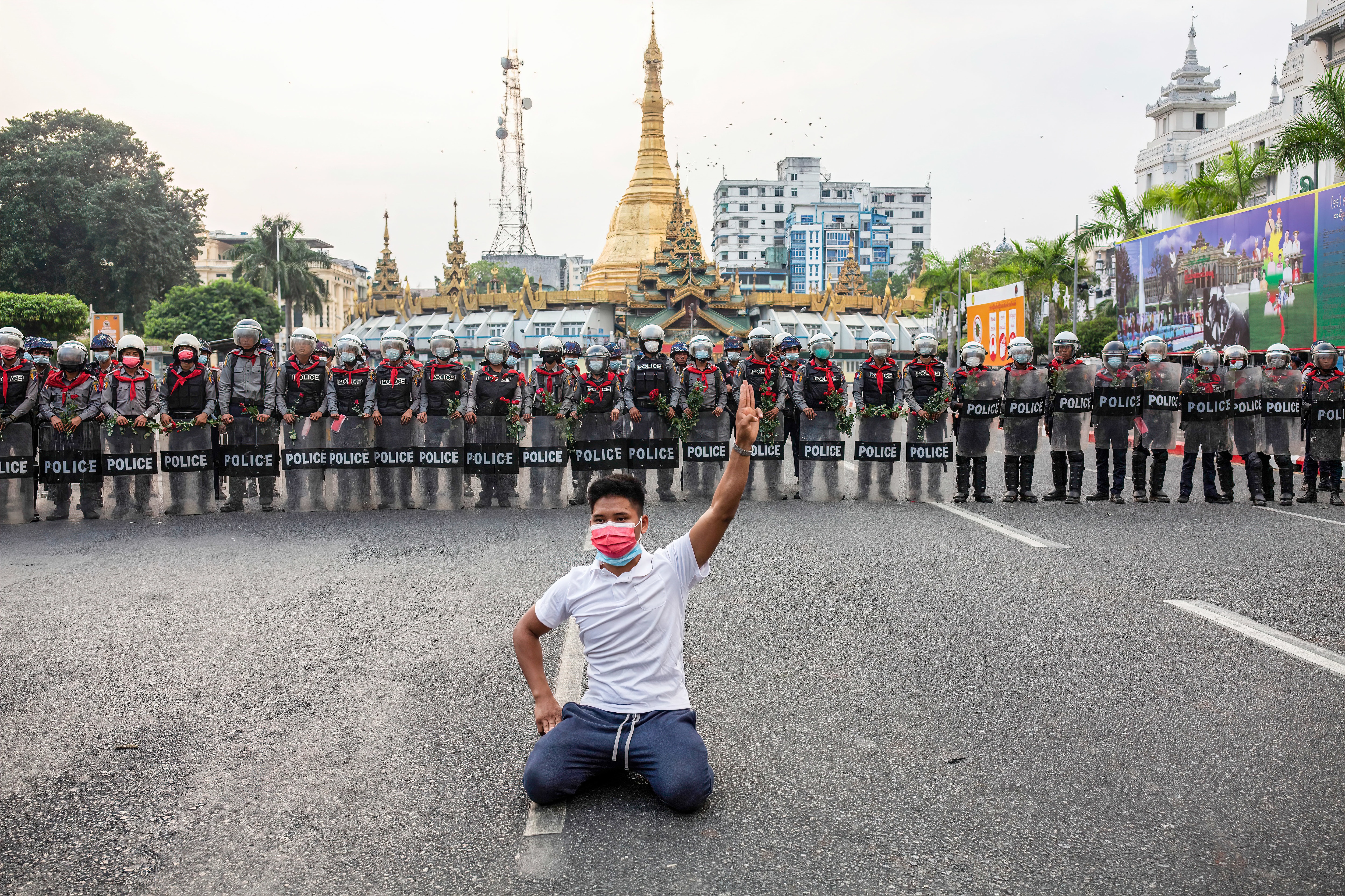 A protester makes the three finger salute with the Sule Pagoda and police officers in the background