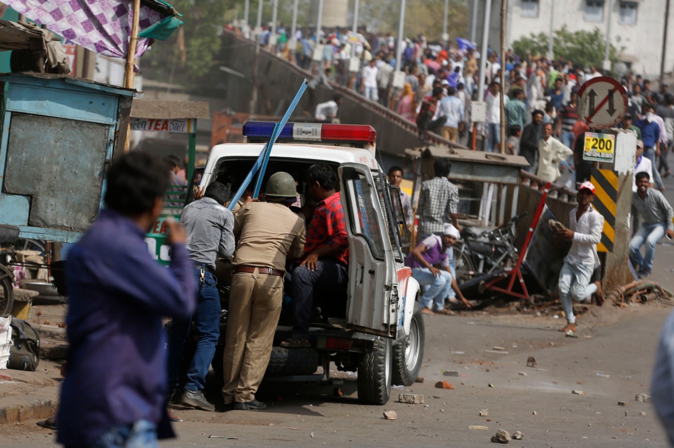 Indian policemen take cover behind a police vehicle as India's lower caste Dalits pelt stones on them during a nationwide strike in Ahmadabad.
